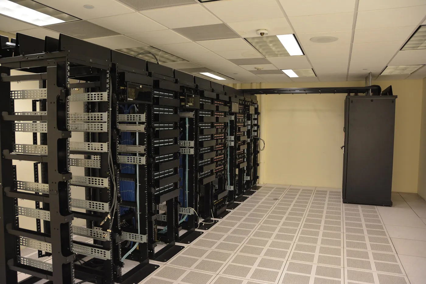 Interieur van een datacenter met meerdere rijen hoge metalen serverracks vol met netwerk- en computerapparatuur.