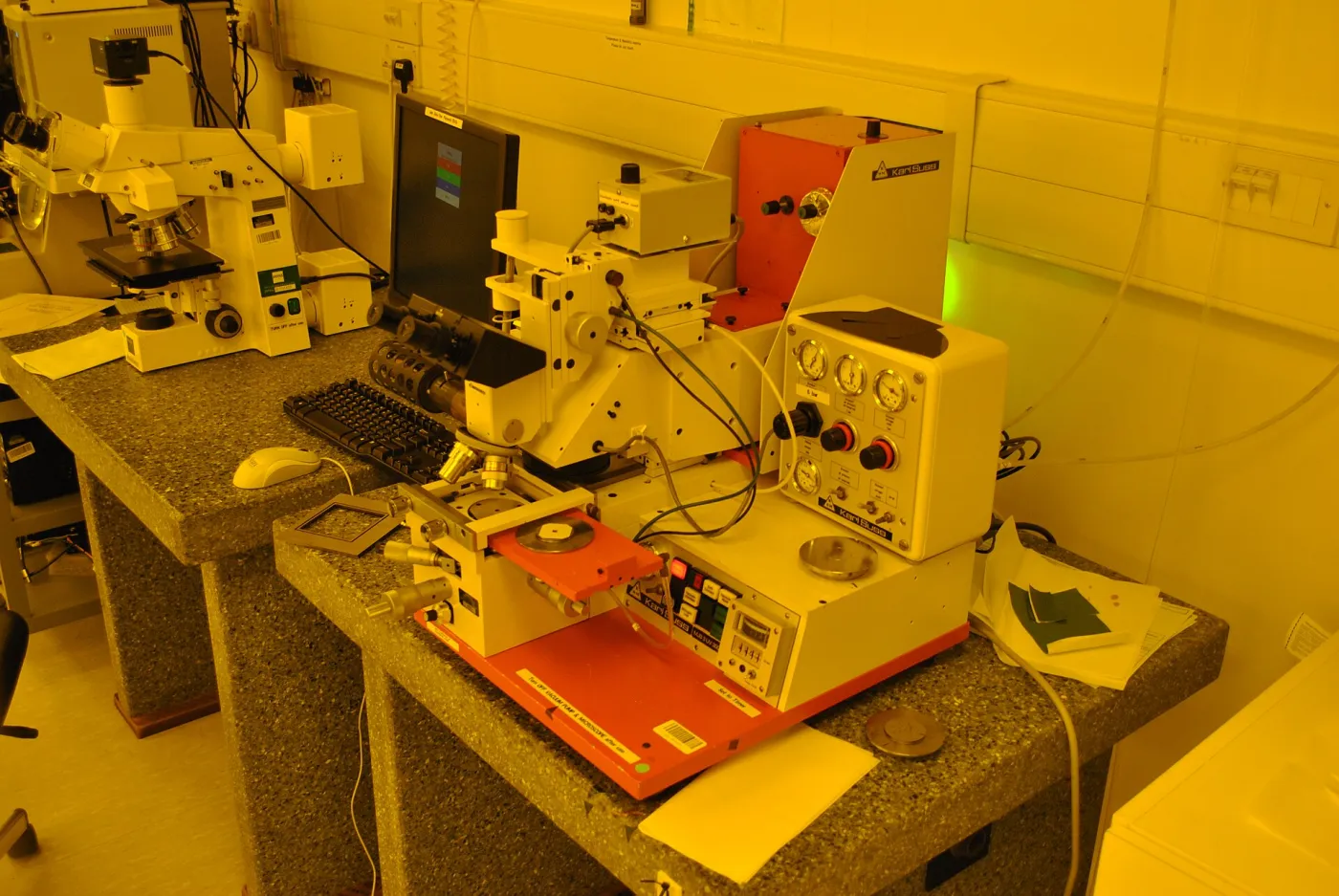 Een fotolithografielaboratorium in een halfgeleider-cleanroom, met gespecialiseerde microfabricage-apparatuur in oranje veiligheidslicht om lichtgevoelige fotoresist te beschermen.